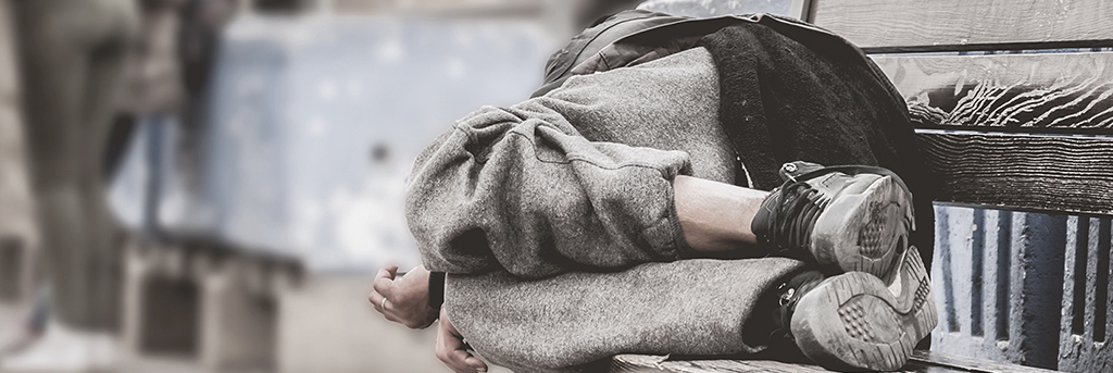 A homeless person sleeping on a bench